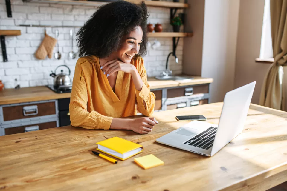 Woman in yellow top sitting at wood kitchen island looking at laptop